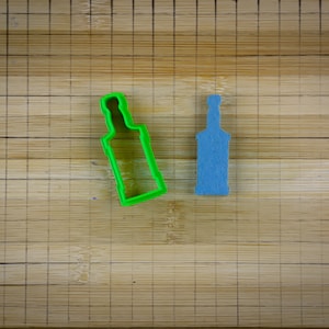May include: Two bottle-shaped cookie cutters on a wooden surface. One is green plastic and the other is blue.
