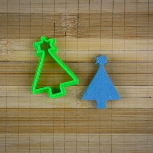 May include: Two Christmas tree cookie cutters on a wooden surface. One is green plastic and the other is blue.