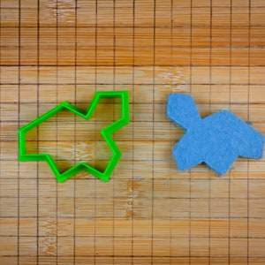 Op de afbeelding: Een groene plastic koekjesvormer in de vorm van een ster en een blauwe stervormige koek op een bamboe snijplank.