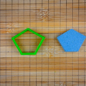 Peut inclure: Un emporte-pièce en forme d'étoile à cinq branches en plastique vert et une étoile à cinq branches en feutre bleu sur une planche à découper en bambou.