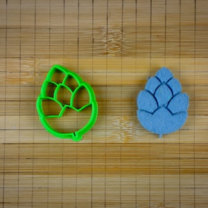 Op de afbeelding: Twee koekjesvormen in de vorm van hop, een groene en een blauwe, op een houten oppervlak.