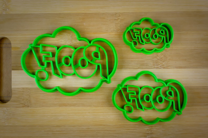 May include: Three green plastic cookie cutters shaped like speech bubbles with the word "FOOD" in a bold, stylized font.
