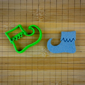 May include: Two elf shoe cookie cutters, one green and one blue, on a bamboo surface.