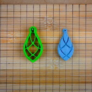 May include: A green plastic mold and a blue plastic impression of a teardrop-shaped ornament with a geometric design.