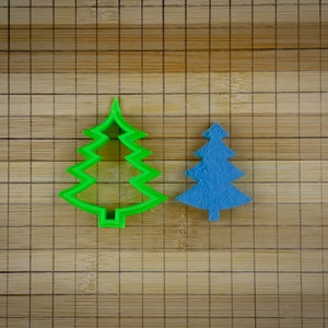Peut inclure: Deux emportes-pièces en forme de sapin de Noël sur une surface en bois. Un emporte-pièce est vert et l'autre est bleu.