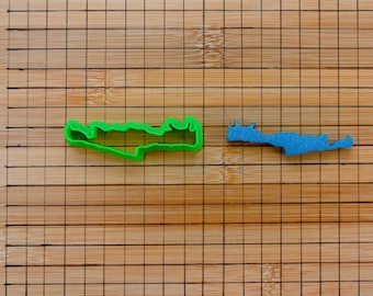 May include: Two cookie cutters, one green and one blue, shaped like islands on a wooden chopping board.