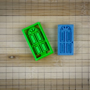 May include: Two door-shaped cookie cutters, one green and one blue, on a bamboo surface.