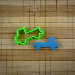 May include: Two plastic cookie cutters shaped like pickup trucks. The larger cutter is green and the smaller cutter is blue.