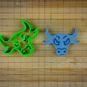 May include: Two bull cookie cutters, one green and one blue, on a wooden surface.