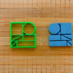 May include: Two geometric shapes, one green and one blue, on a wooden surface. The shapes are made of plastic and have a variety of cutouts.