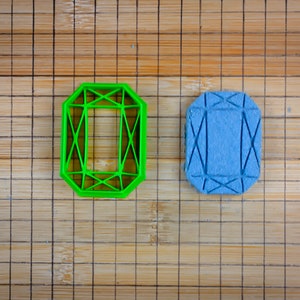 May include: Two diamond-shaped cookie cutters, one green and one blue, on a bamboo chopping board.