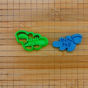 Può includere: Due formine per biscotti su una superficie di legno. Uno è verde e a forma di nuvola con la scritta "Hello Fall" al contrario. L'altro è blu e a forma di nuvola con la scritta "Hello Fall".