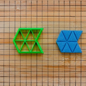 Pode incluir: Dois cortadores de biscoitos geométricos, um verde e outro azul, sobre uma tábua de cortar de madeira. O cortador verde tem a forma de uma flecha apontando para a esquerda, e o cortador azul tem a forma de uma flecha apontando para a direita.