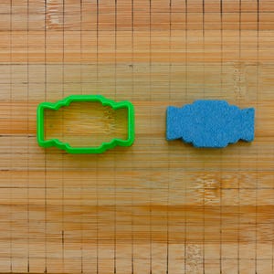 Może przedstawiać: Zielona plastikowa foremka do ciasteczek w kształcie muszki obok niebieskiej foremki do ciasteczek w kształcie muszki na drewnianej desce do krojenia.