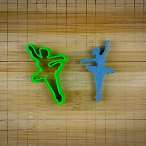 May include: Two ballerina cookie cutters, one green and one blue, on a wooden surface.