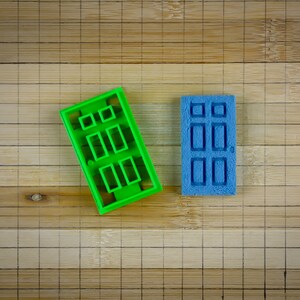 May include: Two plastic cookie cutters shaped like doors. The cutter on the left is green and the cutter on the right is blue.