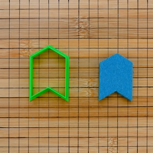 Könnte beinhalten: Zwei Ausstecher auf einer Holzoberfläche. Der Ausstecher links ist grün und hat die Form eines Banners. Der Ausstecher rechts ist blau und hat die Form eines Banners.