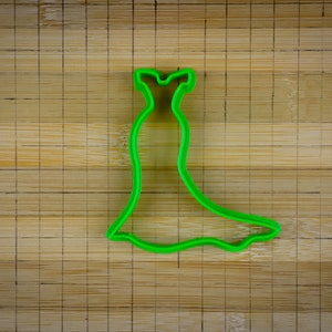 May include: Green plastic cookie cutter shaped like a dress with a long skirt.