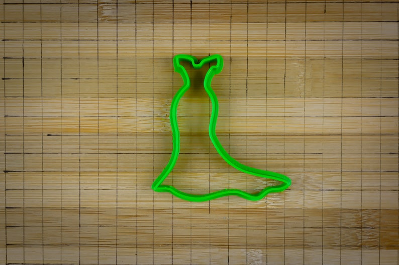 May include: Green plastic cookie cutter shaped like a dress with a long skirt.