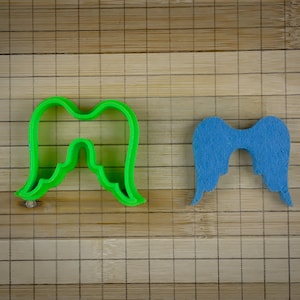 Può includere: Due forme di ali d'angelo, una verde e una blu, su una superficie di bambù.