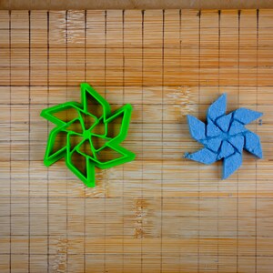 Puede incluir: Un cortador de galletas de plástico verde en forma de molinillo y un molinillo azul hecho de plastilina sobre una tabla de cortar de bambú.