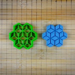 Puede incluir: Dos cortadores de galletas en una tabla de cortar de madera. El cortador de la izquierda es verde y el de la derecha es azul. Ambos cortadores tienen forma de estrella con un patrón geométrico.