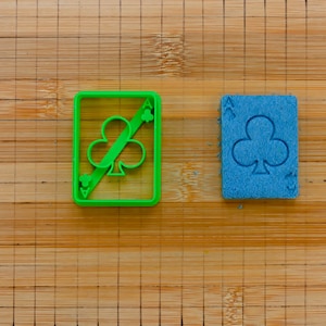 Könnte beinhalten: Zwei Plastik-Ausstecher in Form von Spielkarten mit einem Kleeblatt-Symbol. Der Ausstecher links ist grün und der rechts ist blau.
