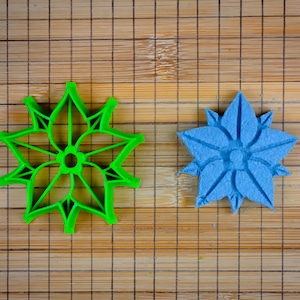 Op de afbeelding: Twee stervormige koekjesvormen, een groene en een blauwe, op een bamboe snijplank.