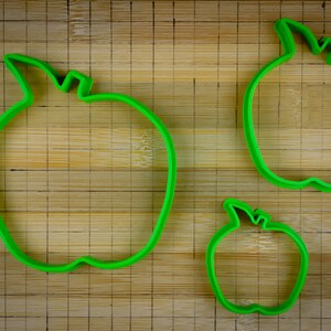 Peut inclure: Trois emportes-pi&egrave;ces en forme de pomme en plastique vert de diff&eacute;rentes tailles sur une planche &agrave; d&eacute;couper en bois.