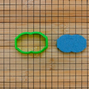 Könnte beinhalten: Zwei Ausstecher auf einem Holzbrett. Der Ausstecher links ist grün und oval mit abgerundeten Kanten. Der Ausstecher rechts ist blau und wolkenförmig.