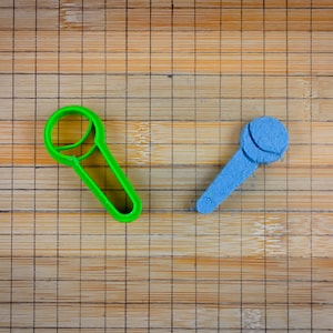 Puede incluir: Dos cortadores de galletas con forma de micrófono, uno verde y otro azul, sobre una tabla de cortar de bambú.
