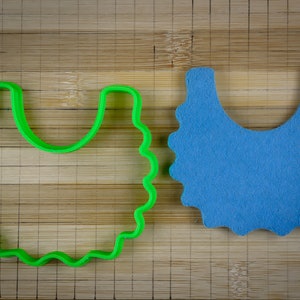 K&ouml;nnte beinhalten: Ein gr&uuml;ner Plastik-Ausstecher in Form einer L&auml;tzchen, neben einem blauen Filz-L&auml;tzchen auf einer Holzoberfl&auml;che.