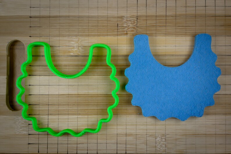 K&ouml;nnte beinhalten: Ein gr&uuml;ner Plastik-Ausstecher in Form einer L&auml;tzchen, neben einem blauen Filz-L&auml;tzchen auf einer Holzoberfl&auml;che.