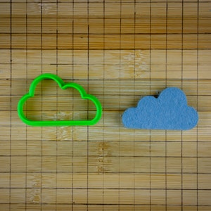 Può includere: Un tagliapasta a forma di nuvola di plastica verde e una nuvola di feltro blu su un tagliere di bambù.