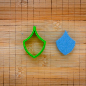 Puede incluir: Un cortador de galletas de plástico verde en forma de lágrima y una lágrima de fieltro azul.