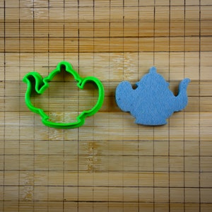 Puede incluir: Dos cortadores de galletas con forma de tetera, uno verde y otro azul, sobre una tabla de cortar de bambú.