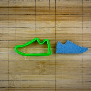 May include: A green plastic cookie cutter shaped like a trainer next to a blue fondant cookie cutter shaped like a trainer.