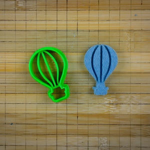 May include: Two hot air balloon cookie cutters, one green and one blue, on a wooden surface.