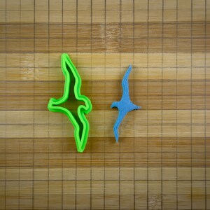 May include: Two bird-shaped cookie cutters, one green and one blue, on a wooden surface.