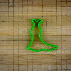 May include: Green plastic cookie cutter shaped like a dress with a fitted bodice and a flowing skirt.
