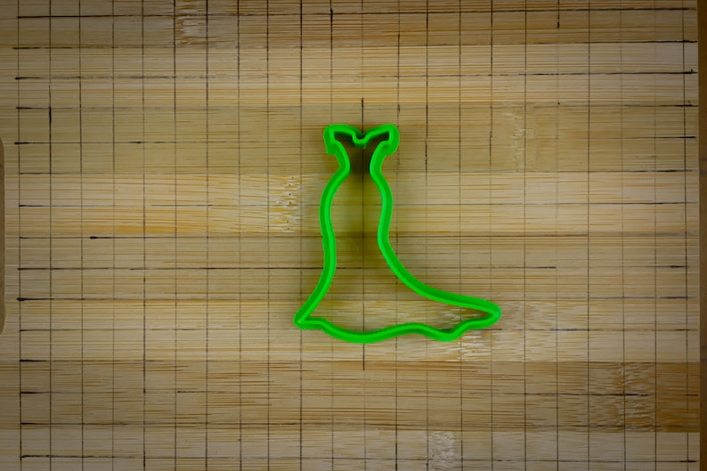 May include: Green plastic cookie cutter shaped like a dress with a fitted bodice and a flowing skirt.
