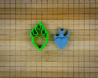 May include: Two heart-shaped cookie cutters, one green and one blue, with flames on top. Both cutters are on a bamboo cutting board.