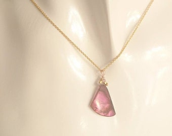 May include: A gold chain necklace with a pink and green gemstone pendant. The pendant is shaped like a teardrop and has a gold bead accent.