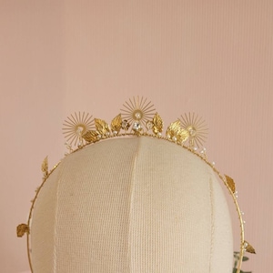 May include: Gold crown with leaf and sunburst details, accented with small white pearls.