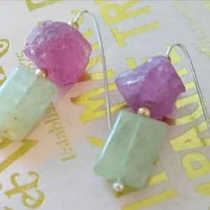 Puede incluir: Un par de pendientes con gotas de piedras preciosas rosas y verdes. Los pendientes están hechos con alambre de plata y tienen detalles dorados.