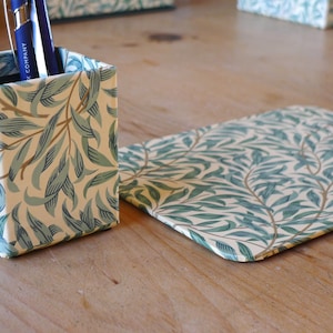 May include: A square, green and white patterned pen holder with two blue pens inside. Next to it is a matching green and white patterned desk mat.