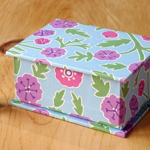 May include: A small blue box with a floral pattern in shades of pink, purple, and green. The box is closed and has a hinged lid.