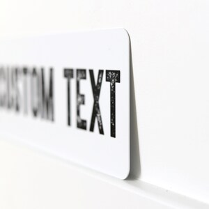 Op de afbeelding: Een wit rechthoekig bord met zwarte tekst die "CUSTOM TEXT" luidt.