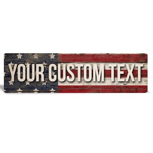 May include: A rectangular wooden sign featuring a distressed American flag pattern with horizontal red and white stripes and a blue field with white stars. The text YOUR CUSTOM TEXT is printed in large, bold, off-white capital letters across the center.