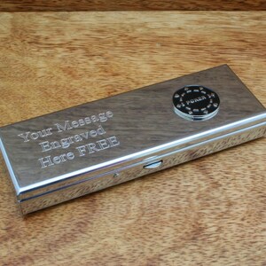 May include: A silver metal poker chip case with a hinged lid. The case has a small round poker chip on the top with the word "Poker" engraved on it. The case has the text "Your Message Engraved Here FREE" engraved on the front.